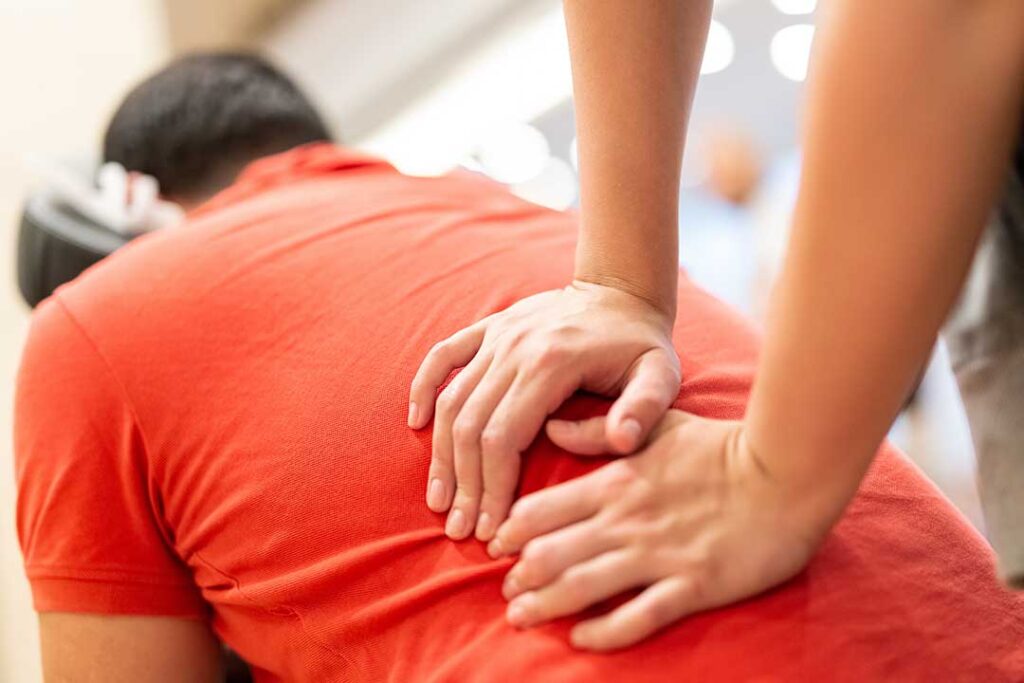 A person sitting on a home sofa, gently massaging their lower back with a concerned expression.